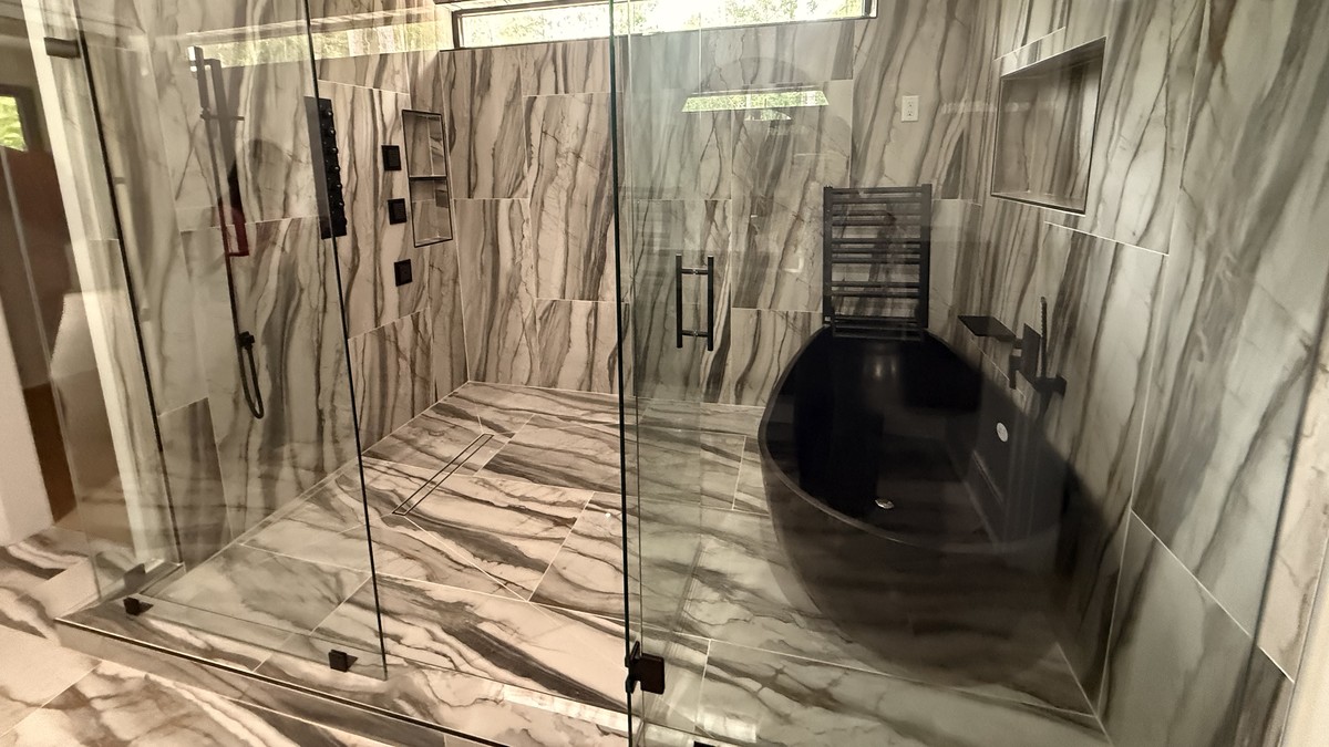 Bathroom with large-format veined tile walls and floor, a frameless glass shower and a black freestanding tub