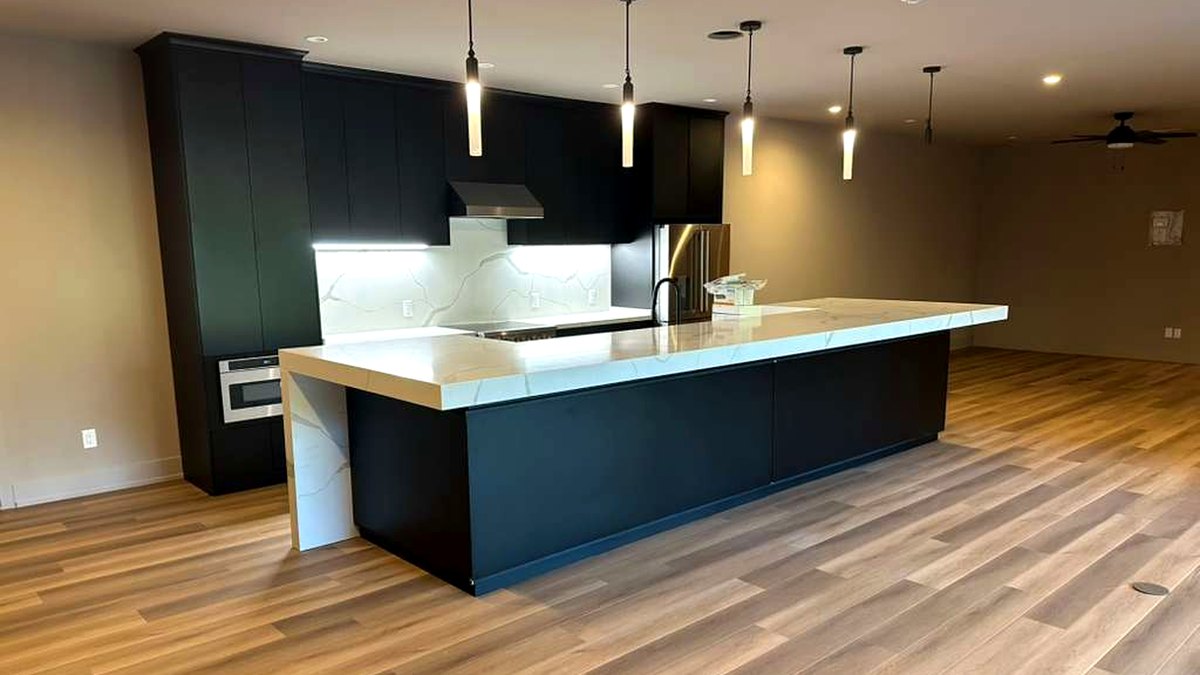 Kitchen with matte navy slab cabinetry, a Calacatta-look quartz waterfall island and wide-plank wood-look LVP flooring