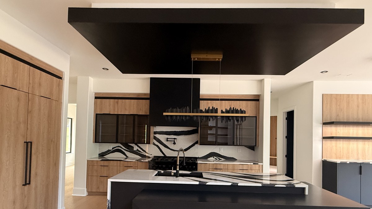 Kitchen with oak woodgrain and matte black slab cabinetry, a black-and-white veined stone backsplash and a black island